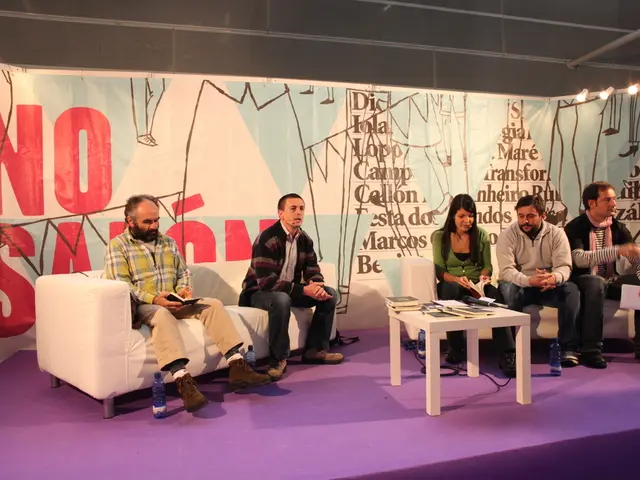 In the image there are few men and women sat on sofa on a stage,in front there is a table on which...