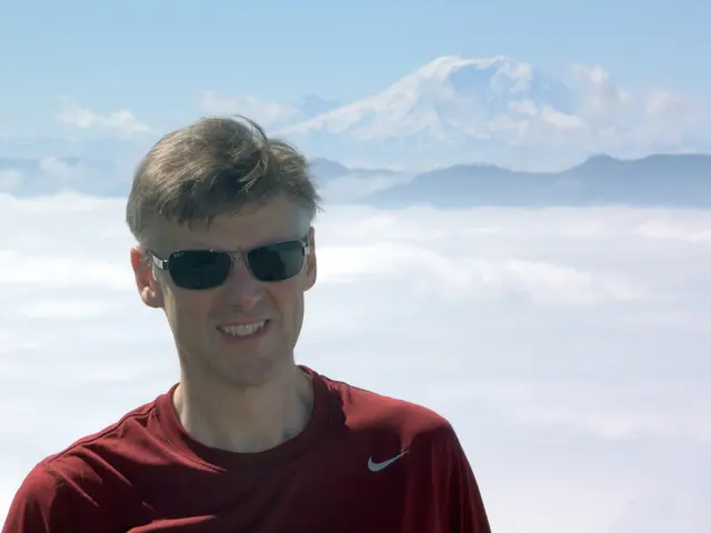 In this picture we can see a man standing in front of ice mountains and smiling at someone.