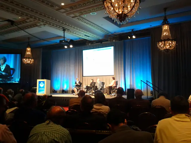 In this picture we can see a group of people sitting on chairs were some are on stage, podium,...