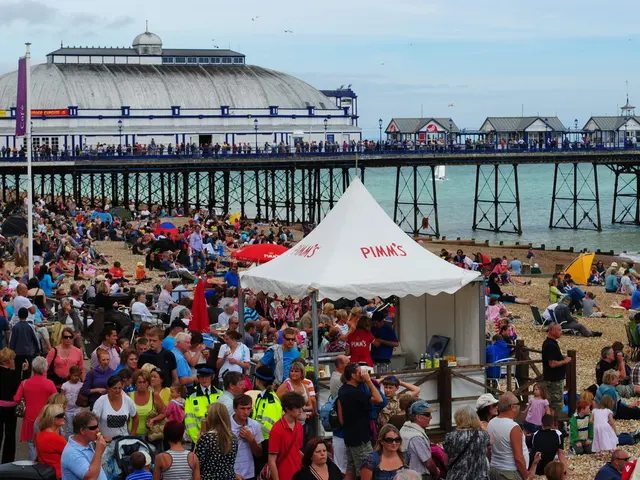 In the image we can see there are lot of people standing on the ground and others are sitting on...