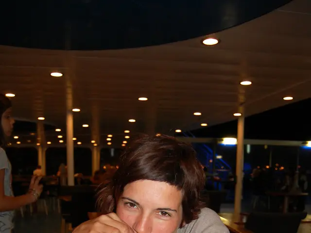 There is a woman sitting on a chair and she is drinking a beer which is on this wooden table. Here...