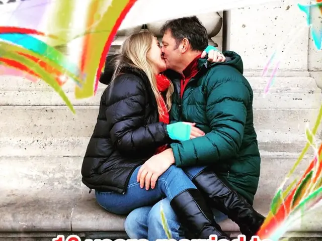 A woman and man are kissing each-other. These two people wore jackets. Something written on this...