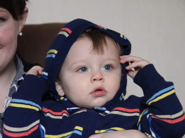 In this image there is a woman holding a child in her arms, behind the woman there is a wall.