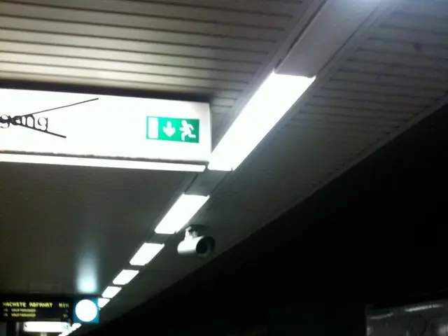 In this image a person is standing on the platform having a name board attached to the wall. There...