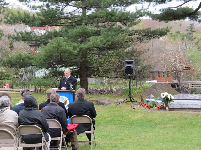 In the image we can see there are people sitting on the chairs and there is a man standing near the...