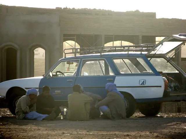 In the center of the image, we can see a vehicle and there are some people sitting on the ground...