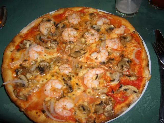 In the image there is a pizza kept on the plate, it has mushrooms, prawns and some other items and...