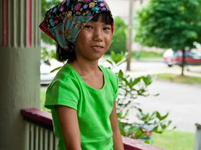 In this image a girl holding a skating board visible in front of fence there is a pillar visible on...