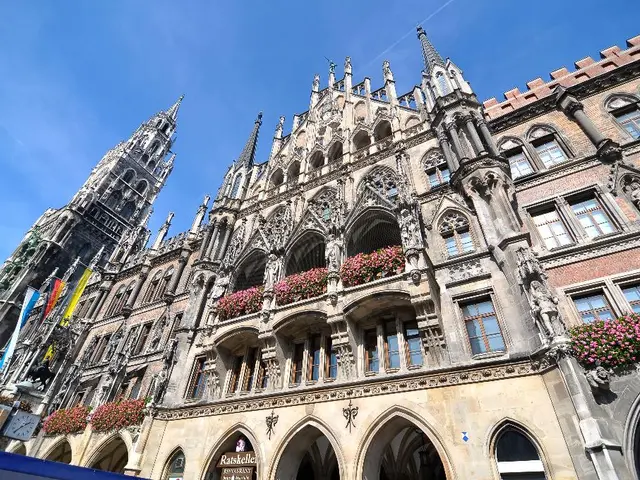 In this image I see a building and I see a tower over here and I can also see the flags and flowers...