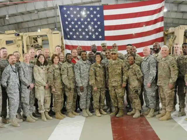 In this image there are group of people standing and smiling , and in the background there is a...