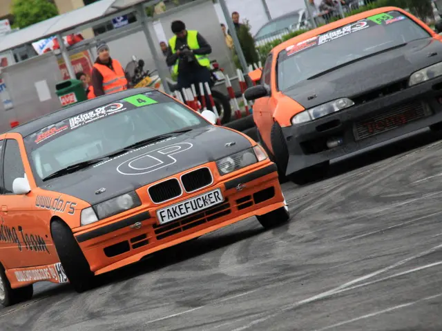 In the image there are two cars drifting on the road, behind it there are few men standing in front...