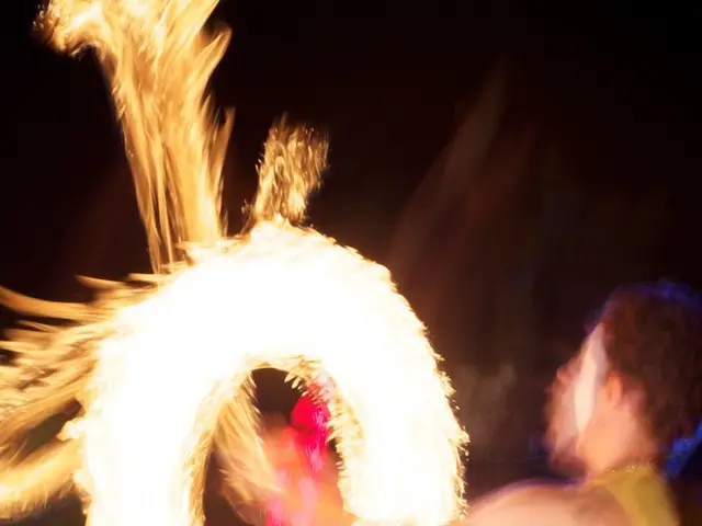 In this image there is a man who is playing with the fire. In the background there are lights.