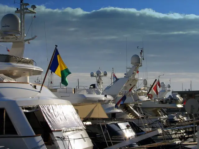 On the left side, there is a white color boat, on which, there is a flag attached, parked along...