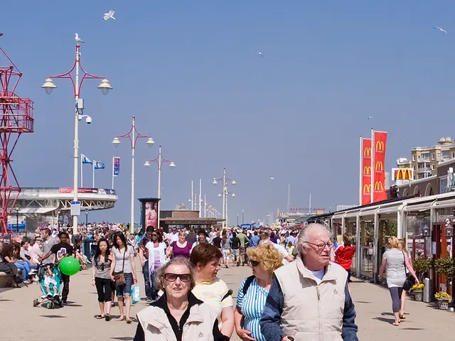 In this image I can see number of people are walking and I can see few of them are carrying bags....