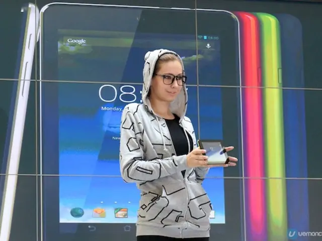 In the image we can see a woman standing, wearing clothes, spectacles and she is smiling, she is...