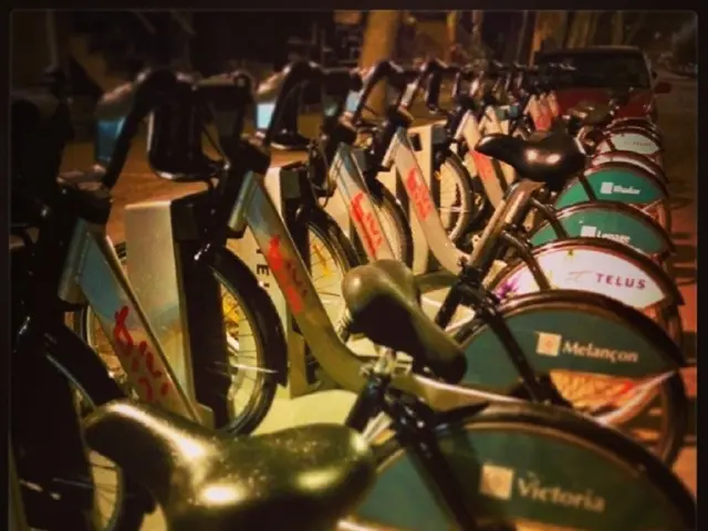 In the middle of the image we can see some bicycles. Behind the bicycles there is a vehicle.