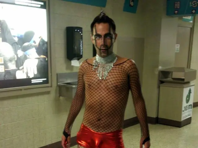 In this picture we can see a man wearing a black netted costume & jewellery and standing on the...