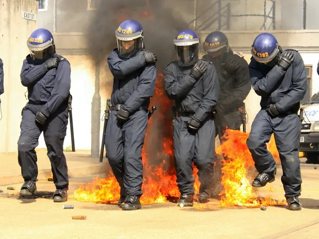 In this image there are people wearing helmets. Behind them there is a fire. There are a few...