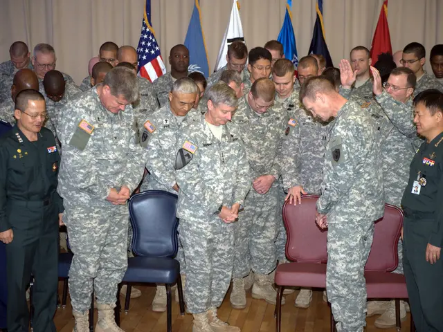These group of people are standing, in-between of them there are chairs in red and blue color. Most...
