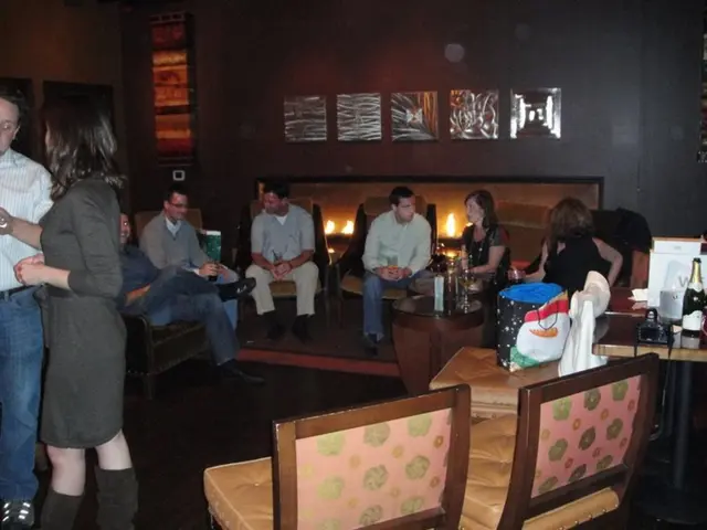 A group of people sitting in chairs are talking to each other. There is couple standing aside.