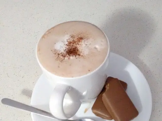 In the middle of this image, there are a cup having coffee, two biscuits and a steel spoon placed...