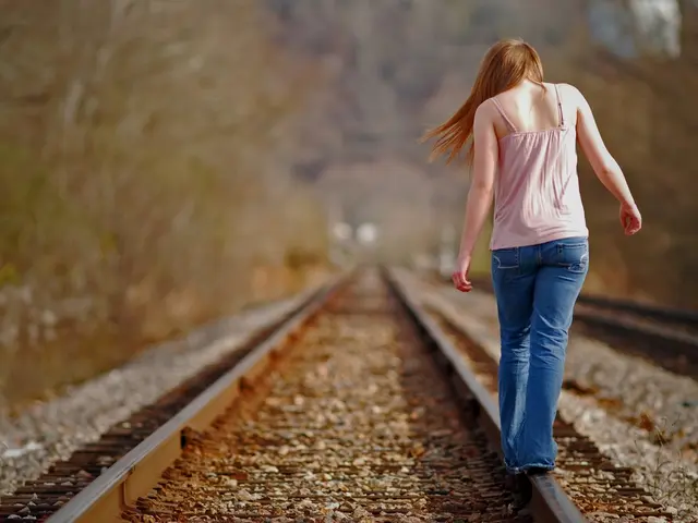 In this image we can see a woman walking on the railway track and a blurry background.