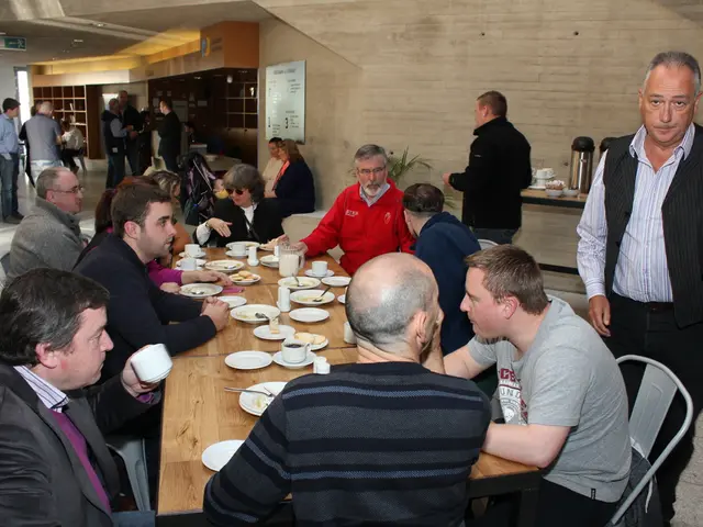 There is a group of people who are sitting on a chair and in front of a wooden table having snacks...