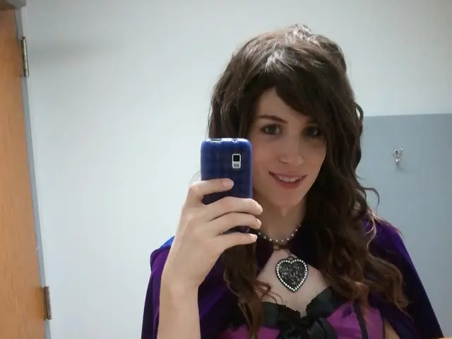 In this image I can see a woman is holding the mobile in her hand, she wore brinjal color top and...