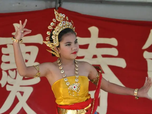 In this image we can see a girl is dancing by wearing cultural dress and jewelry. Behind her one...