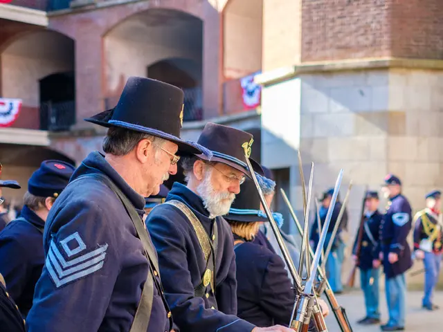 In this image there are a few people standing, in front of them there are guns. In the background...