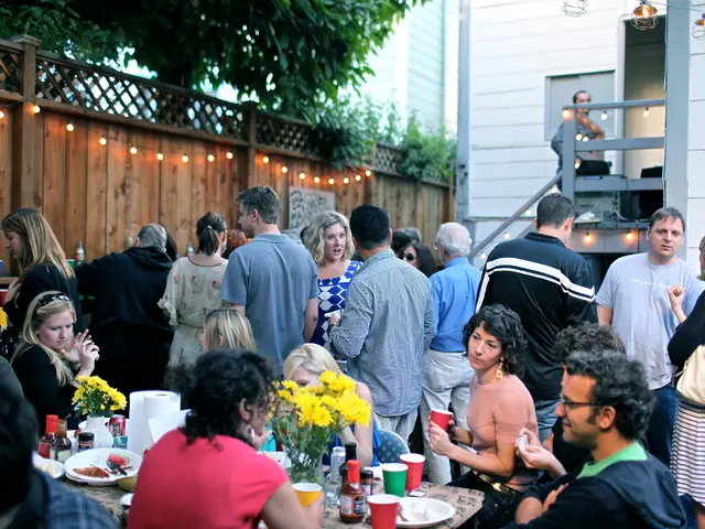 People are at a party. In which some are sitting around a table and some are standing.