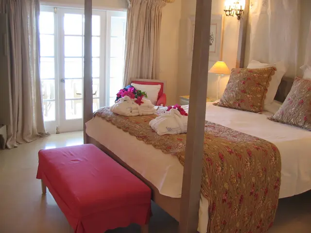 In this image there is a bed, on top of the bed there are pillows and towels, in front of the bed...