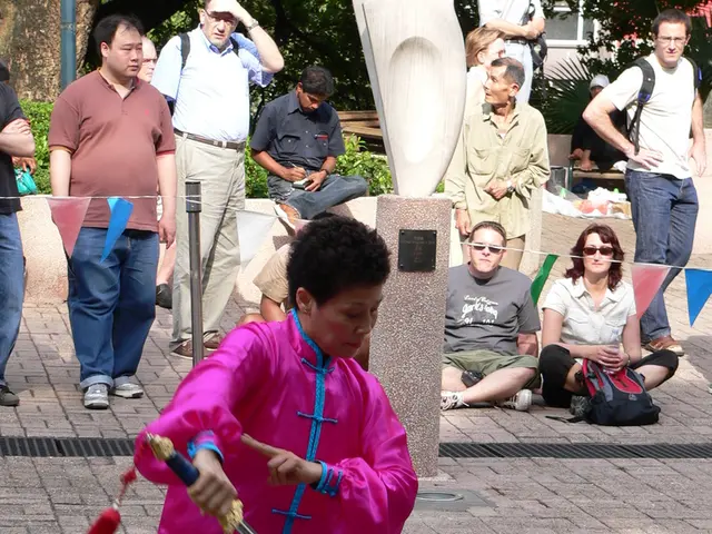 Here a person is holding a sword , this person wore a pink color dress. Many people are observing...