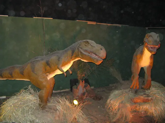 In this picture we can see statues of dinosaurs. There is some dry grass and a light on the path....