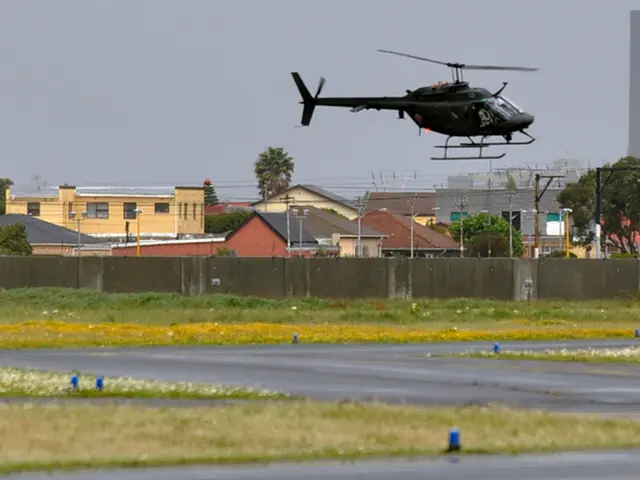 In the image there is a road and around the road there is some grass and there is a helicopter in...