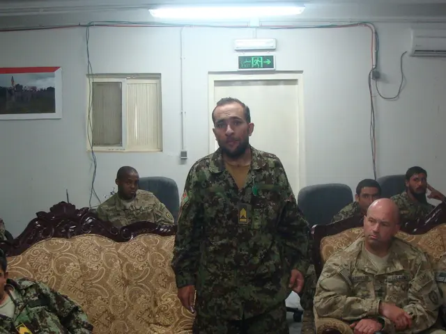 In this picture we can see some army people are sitting in the chairs and couch, among them one...