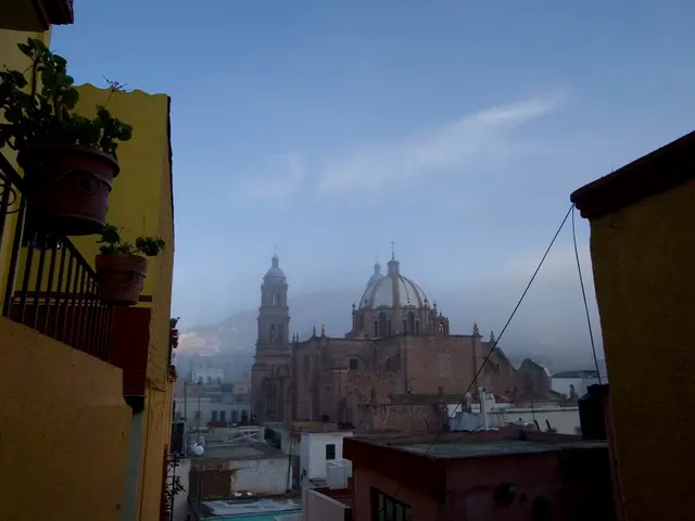 In the image there are many buildings and houses, on the left side there is a wall and above the...