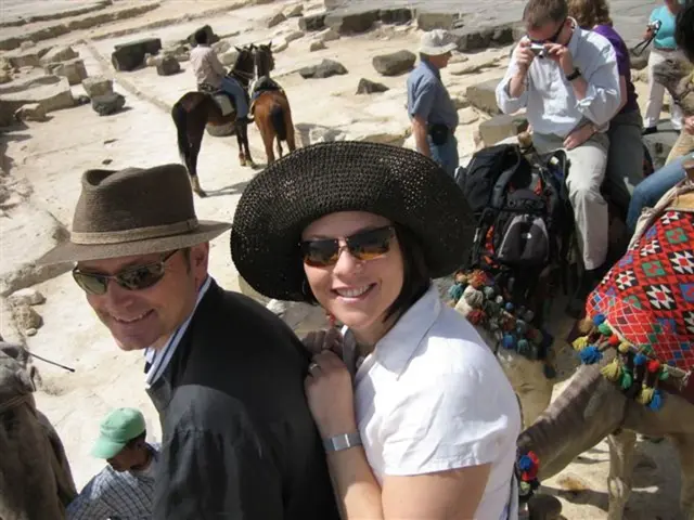 This image consists of so many persons. There are camels in this image. There are persons sitting...