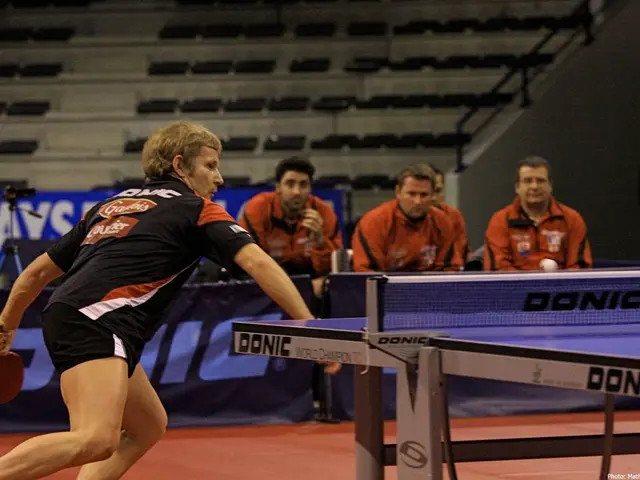 In this image a man holding a table tennis bat in his hand, in front of him there is a table tennis...