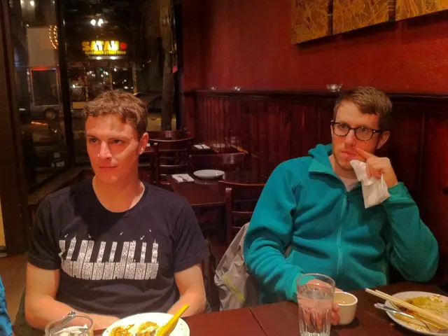 This image is clicked in a restaurant. There are so many tables and chairs. There are two paper...