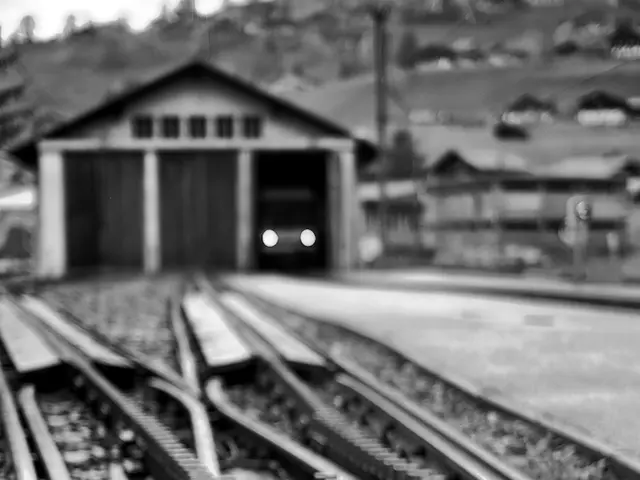 In this picture I can see railway tracks, a shed, vehicle and houses.