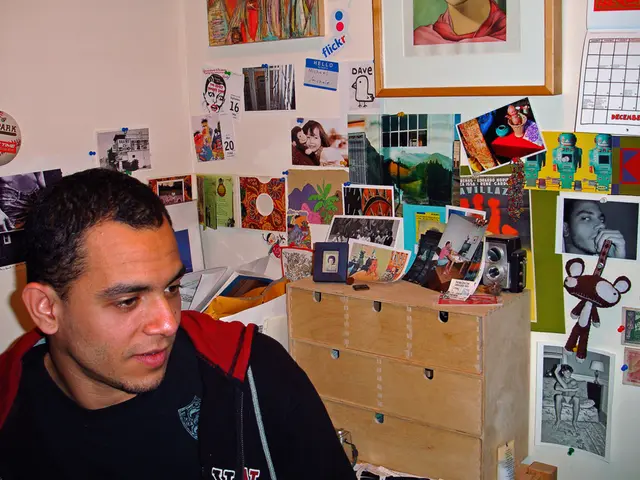 In this image I can see a person sitting on the left. There are many papers attaches on the walls....