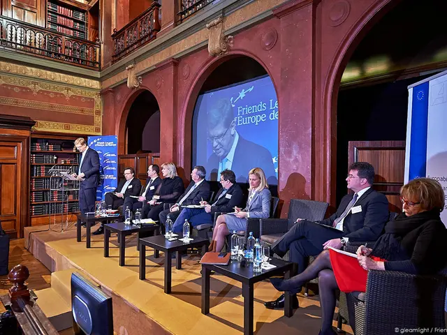 In this image we can see few people are sitting on chair on the stage. This man standing near the...