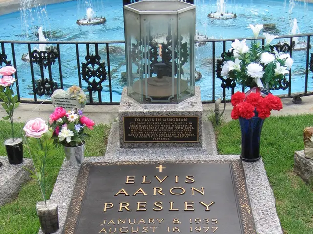 In this image we can see a gravestone, there are flowers, flower pots and a doll on the gravestone...