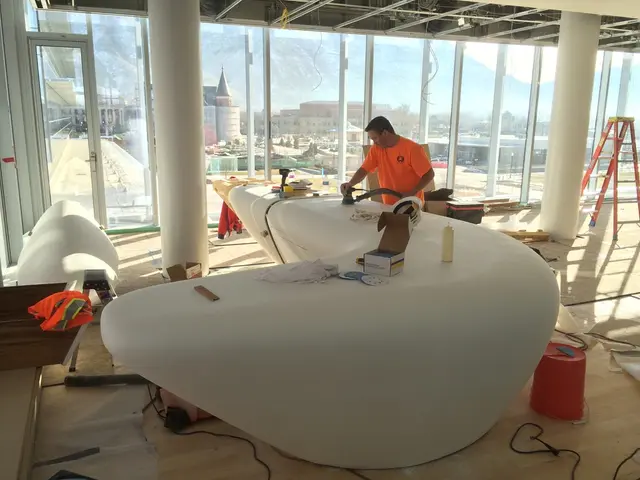 The person wearing orange shirt is working and there are buildings in the background.