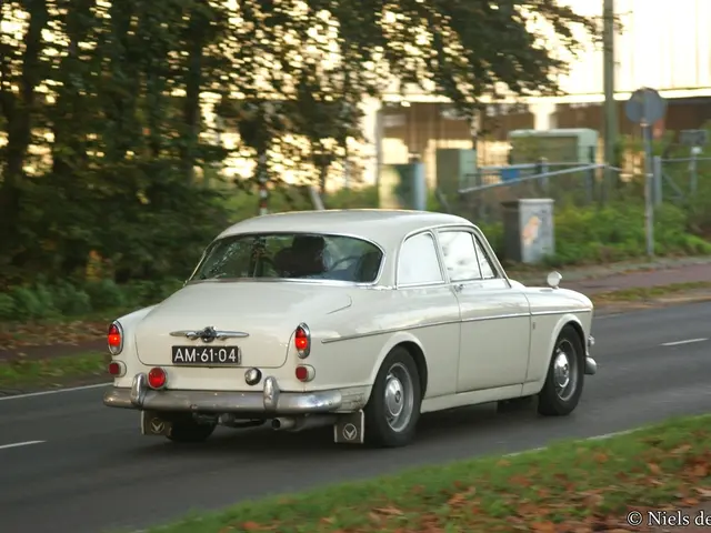 In this image there is a white ambassador car on the road. In the background there are buildings....