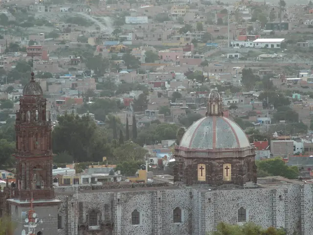 The image is an aerial view of a city. In the image we can see trees, buildings, roads, poles and...