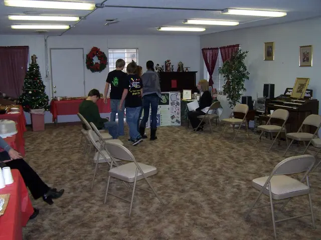 There are many chairs, tables in this room. There are some persons standing and some are sitting....