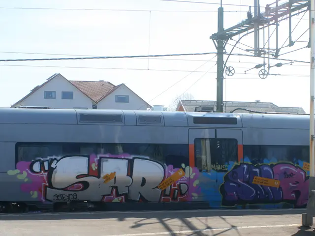 Graffiti is on the train. These are cables. Background there are houses with windows.