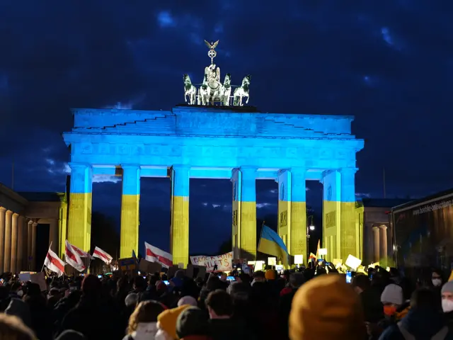 The image shows a crowd of people standing in front of the Brandenburg Gate in Berlin, Germany,...